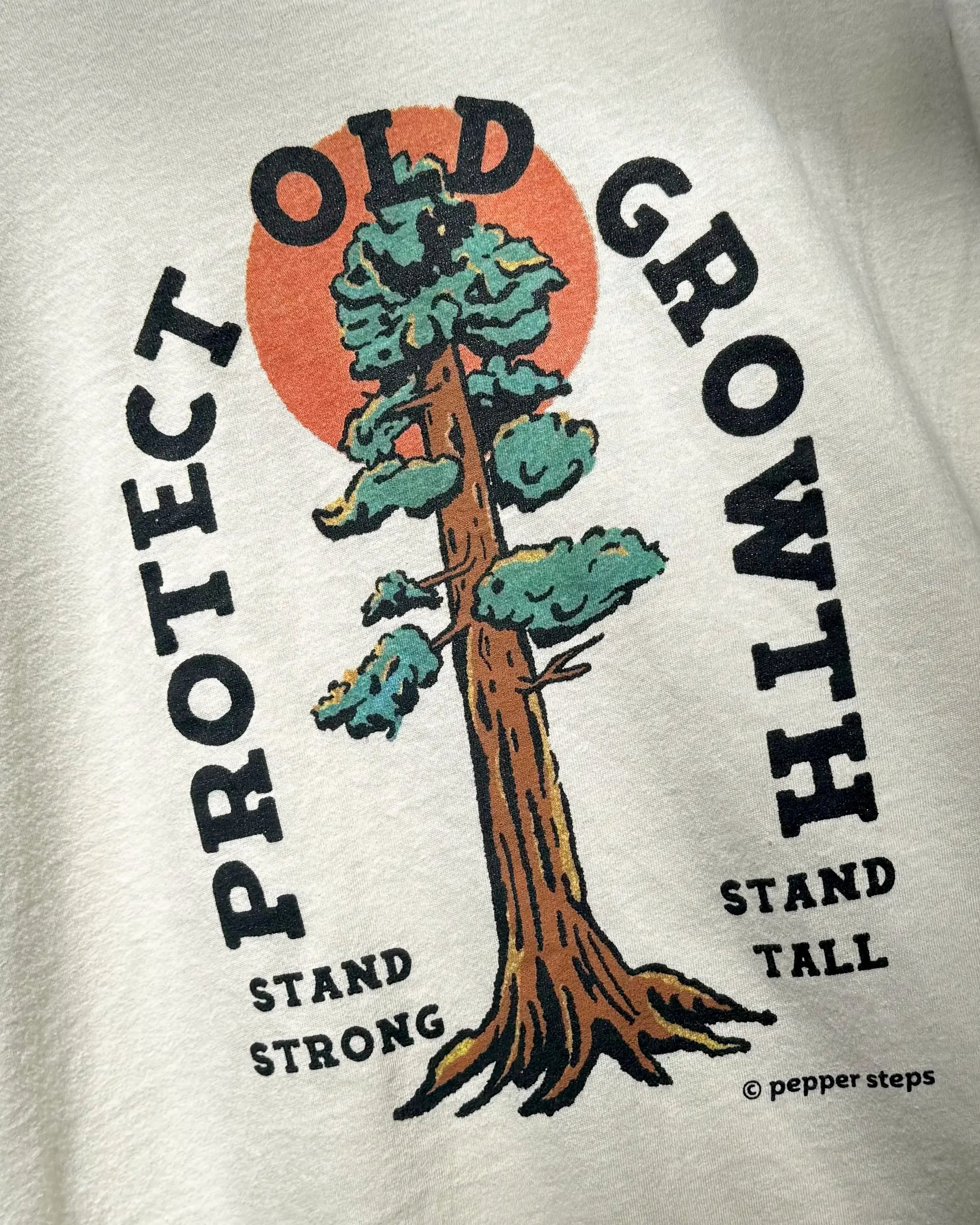 T-shirt with a graphic of a tree and text 'Protect Old Growth Stand Strong Stand Tall' on a light gray background.